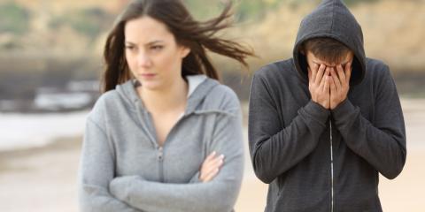 Young woman with arms crossed turned away from young man with face in his hands.