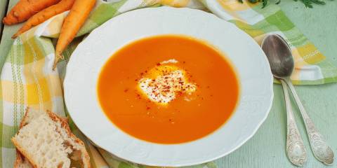 A bowl of carrot and apple soup with bread on the side