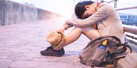 An exhausted woman sitting against a railing with her head on her knees