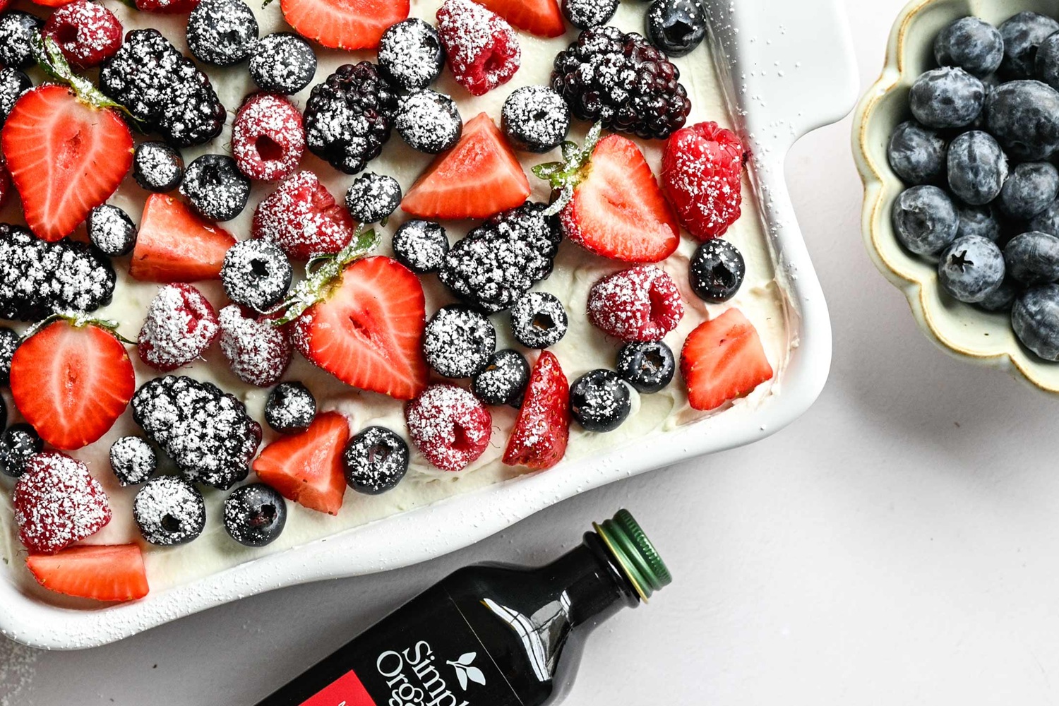 berries on tiramisu with powdered sugar on them also bottle of vanilla extract