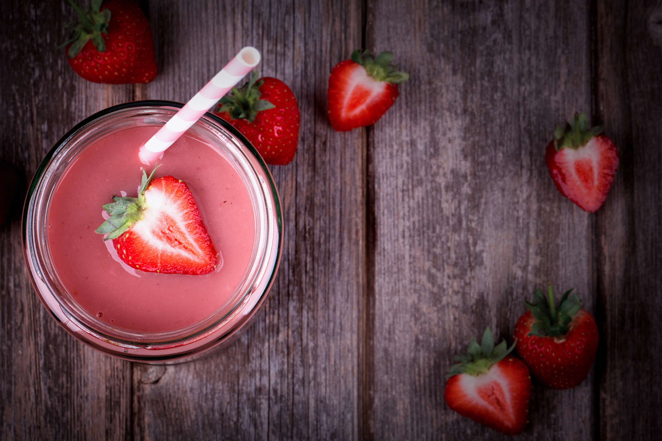 A glass of strawberry smoothie on weathered picnic table wood.