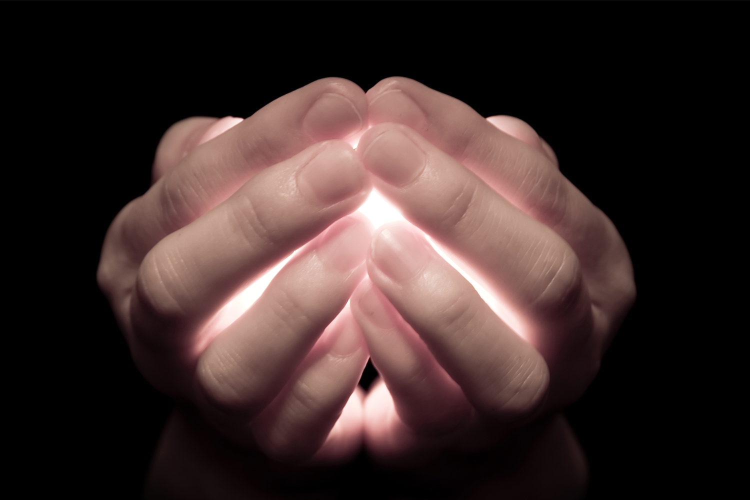 hands clasping a glowing light in the dark
