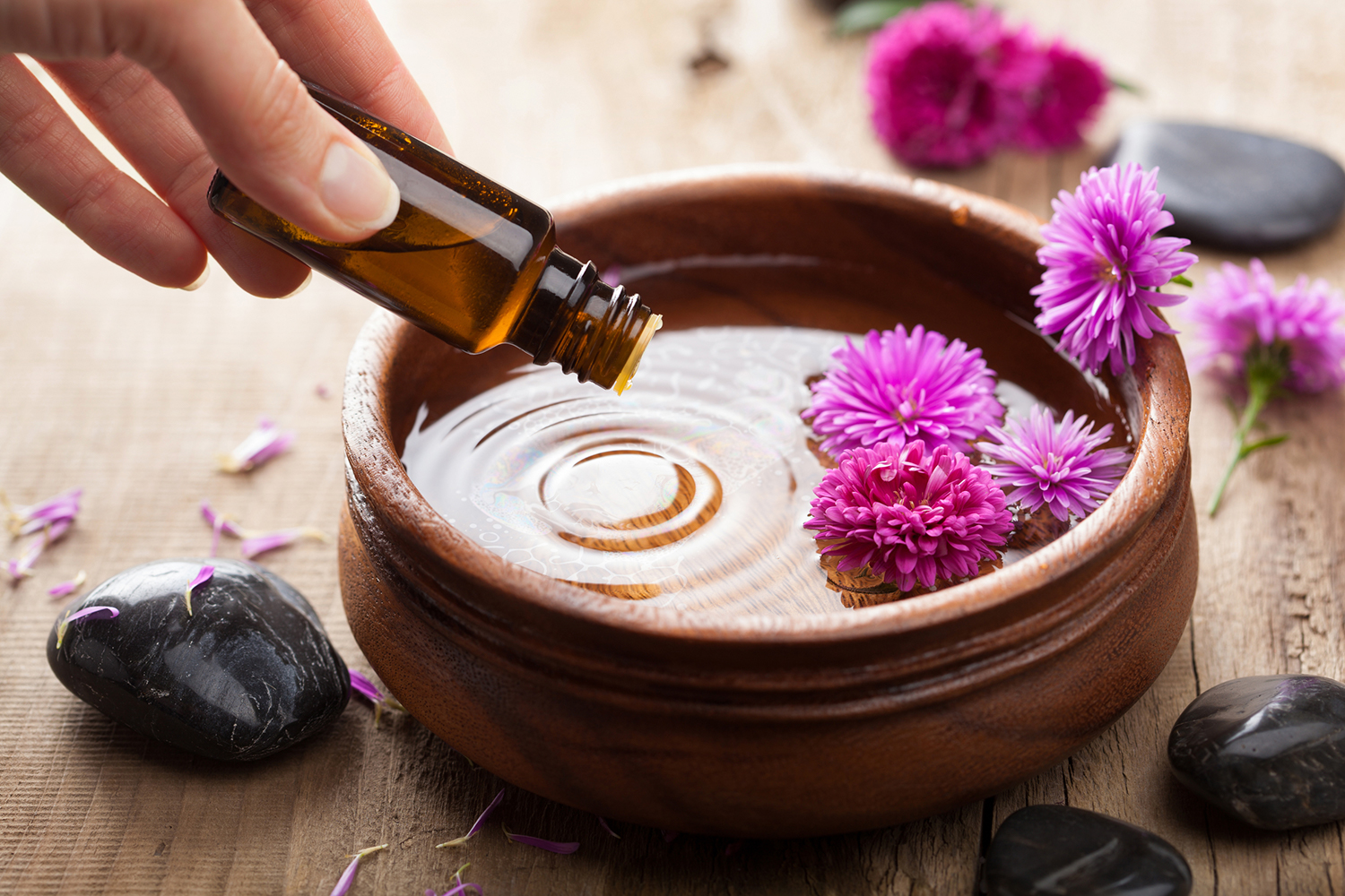 Essential oil being dripped in to a wooden dish for aromatherapy.