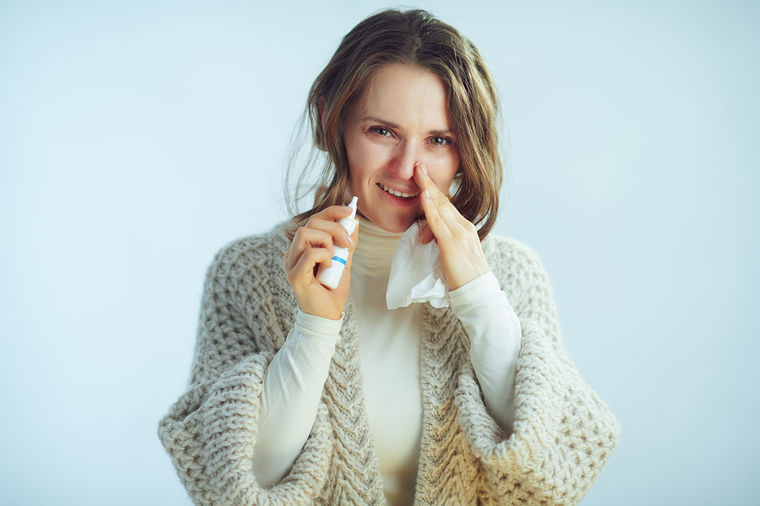 a middle-aged woman with tissues and nasal spray