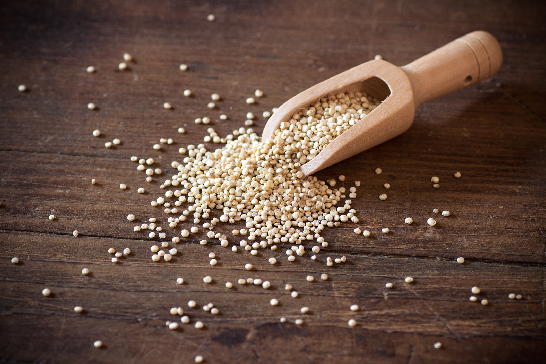 A scoop spilling quinoa out onto a wooden table.