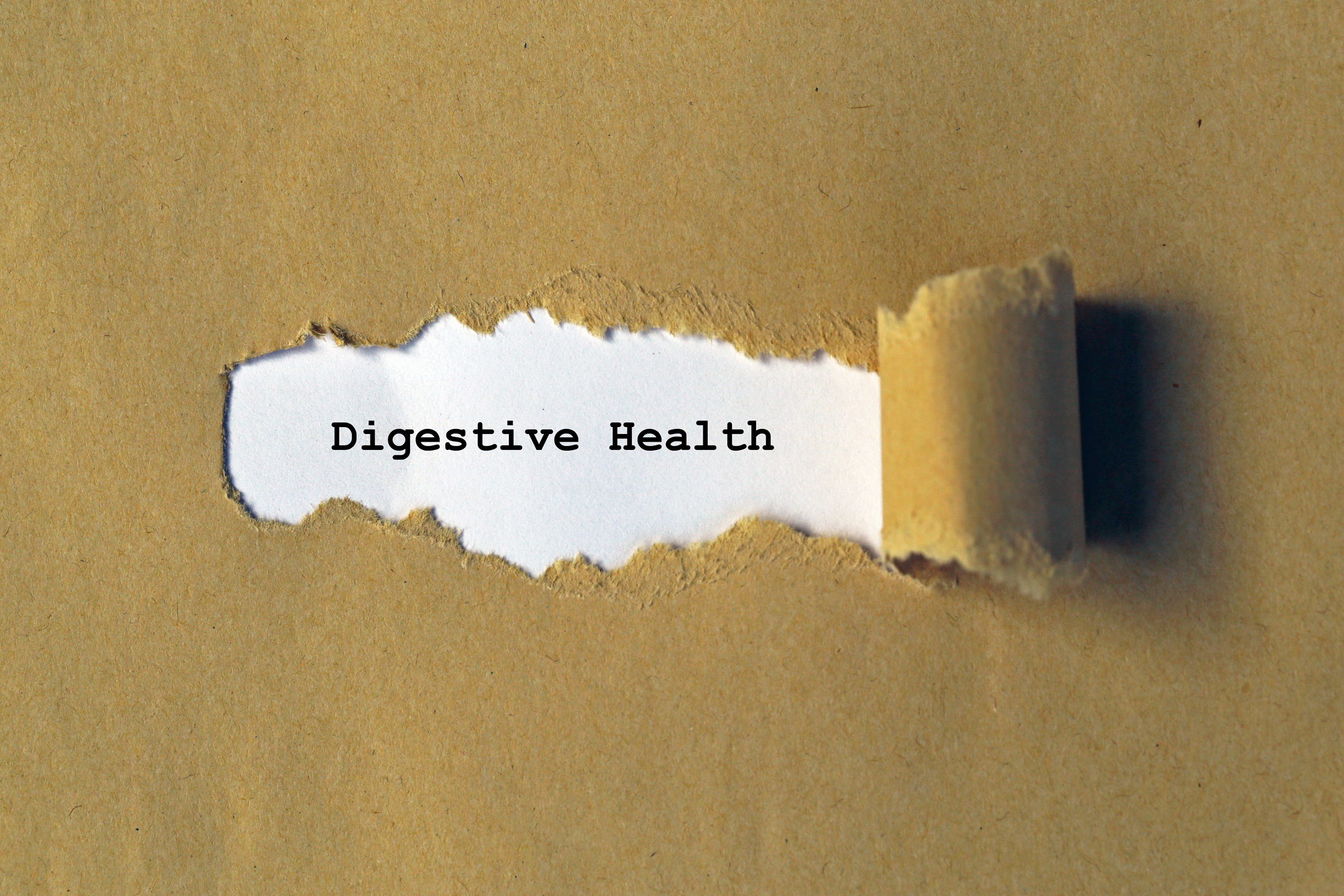 Brown paper ripped to reveal the words digestive health typed on white paper beneath.