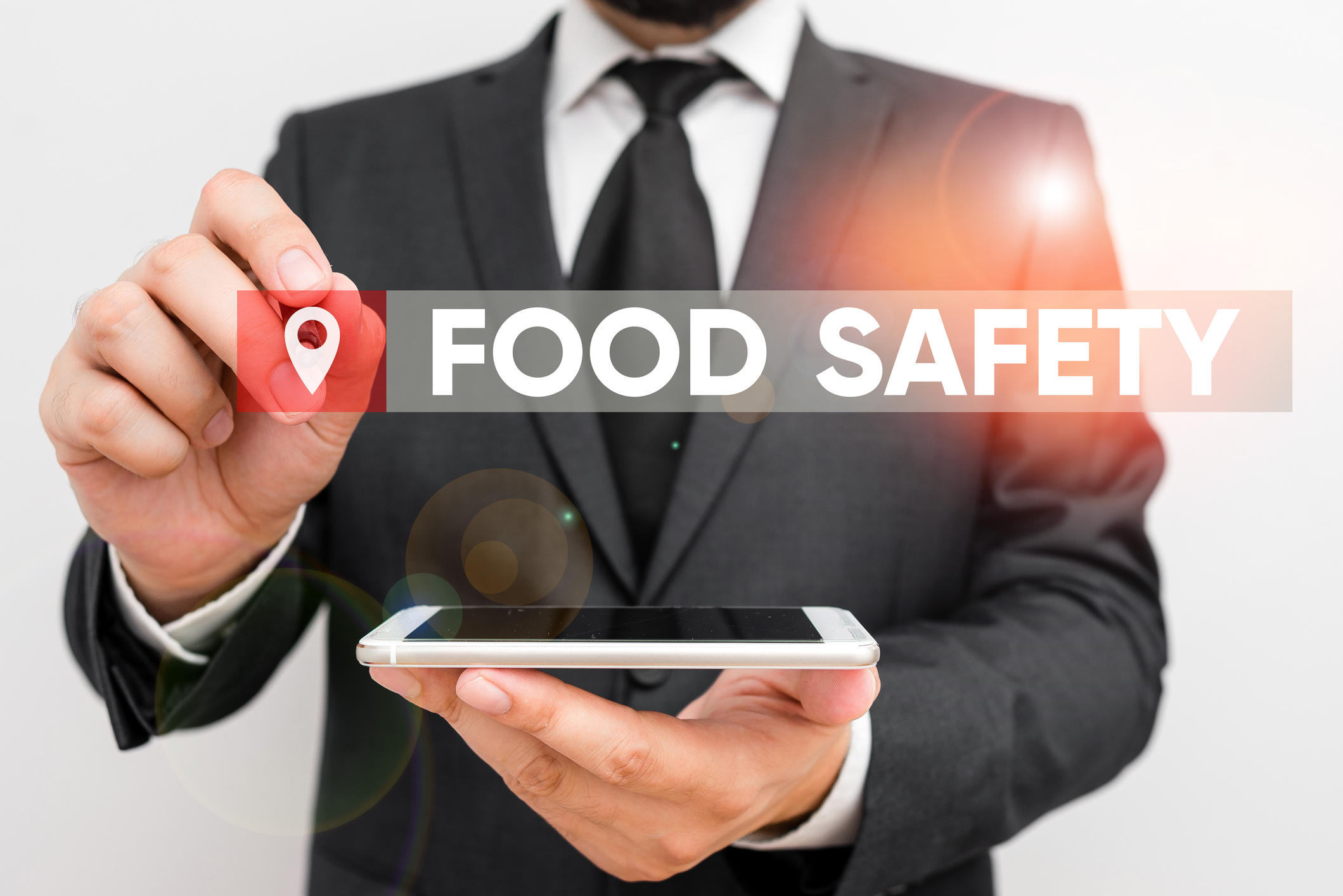 Man in suit holds cell phone flat in one hand and with other is pointing to the words Food Safety