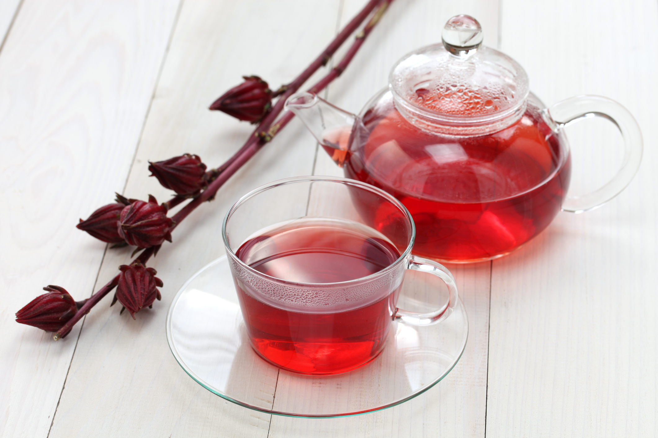 Hibiscus tea in a glass cup in front of a glass tea kettle. 