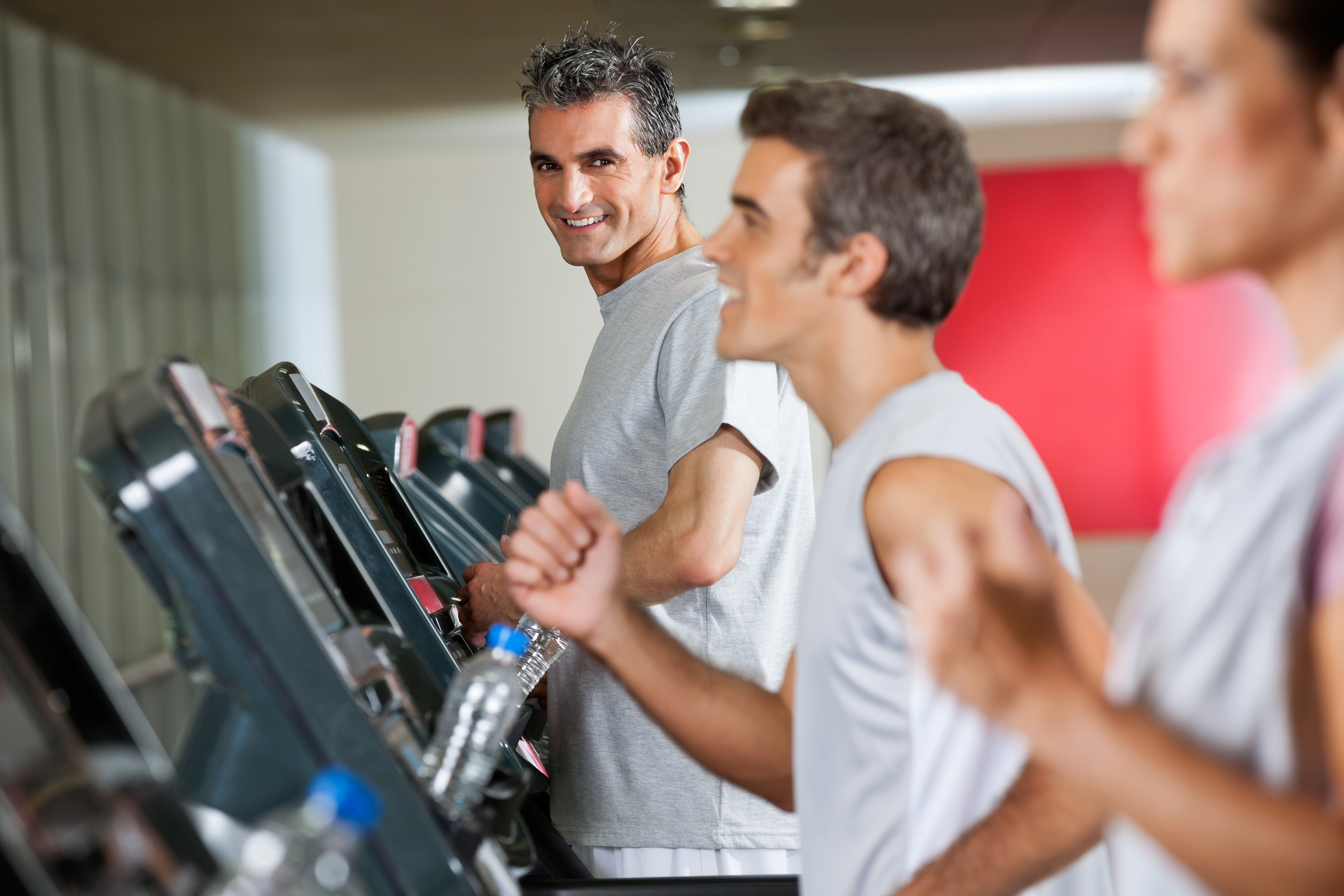 Middle aged man on a treadmill smiling at a younger male on another treadmill