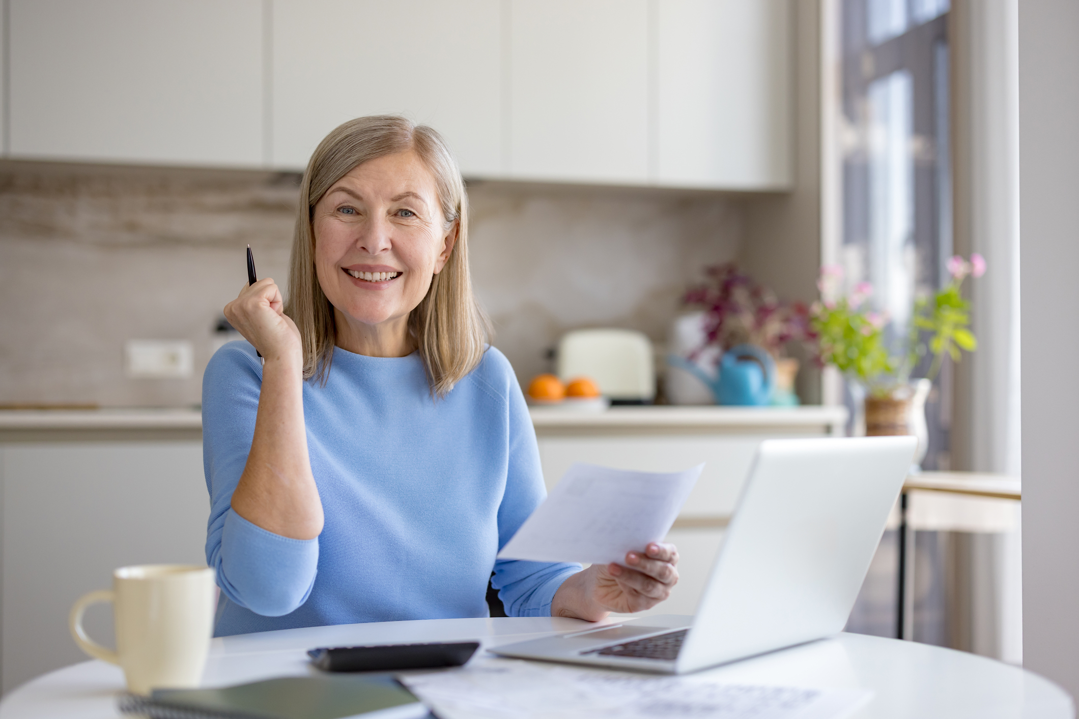 Middle-aged woman working happily in front of a computer in her kitchen.