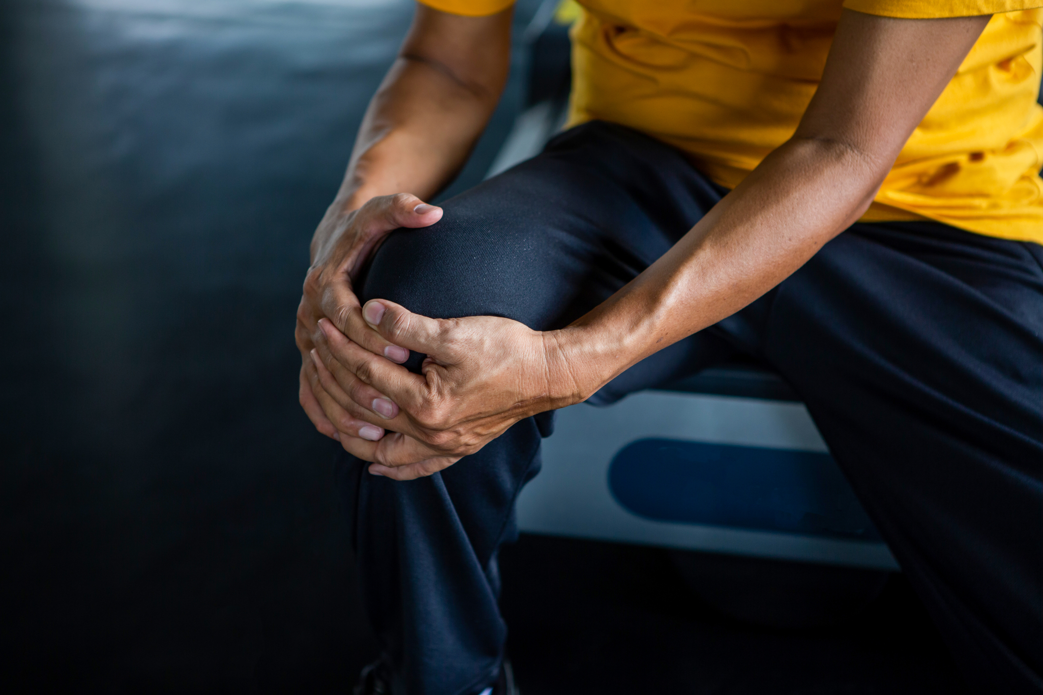 Senior Asian man in work-out gear holding an aching knee.