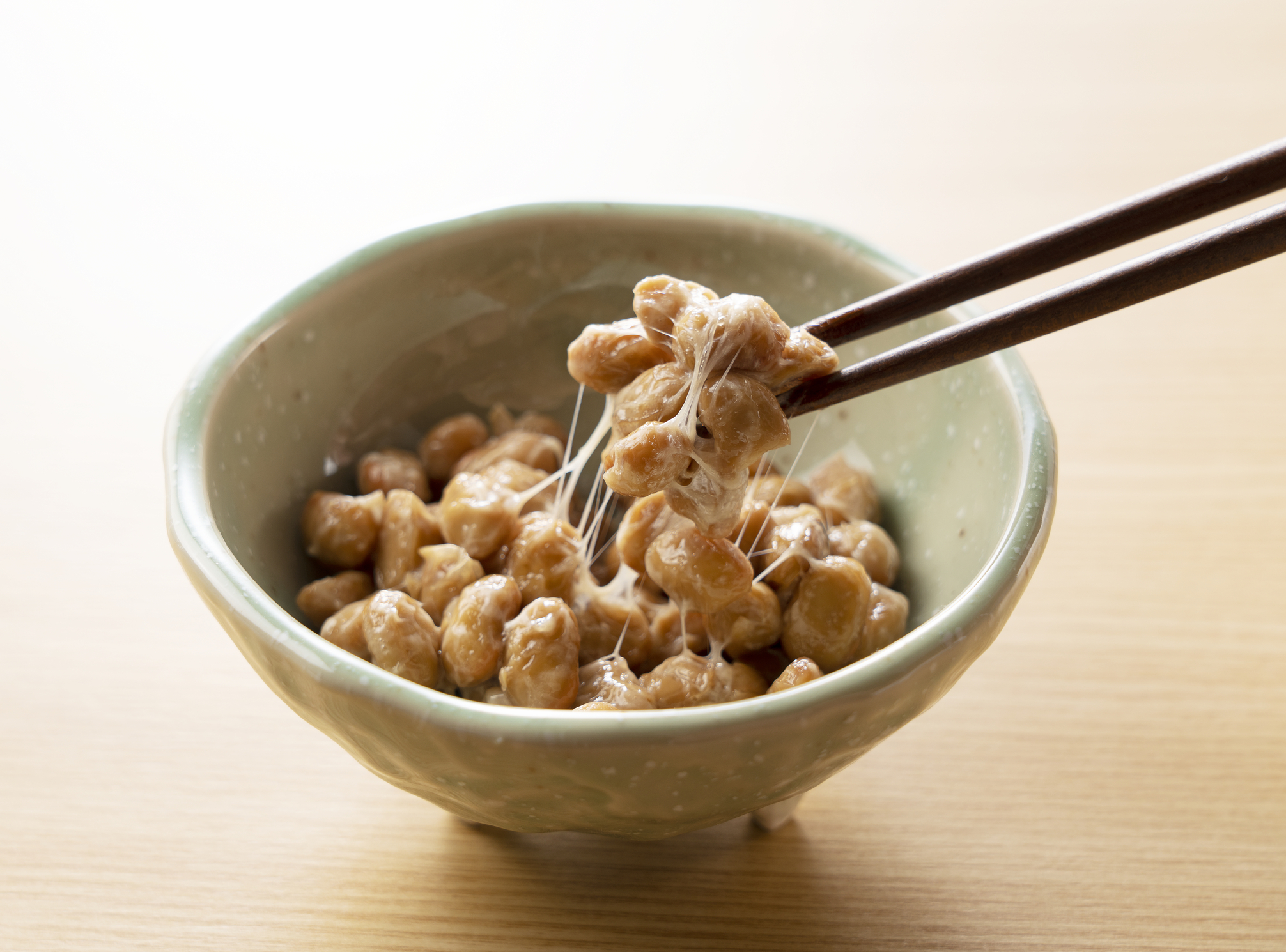 Chopsticks picking up some natto from a small bowl.