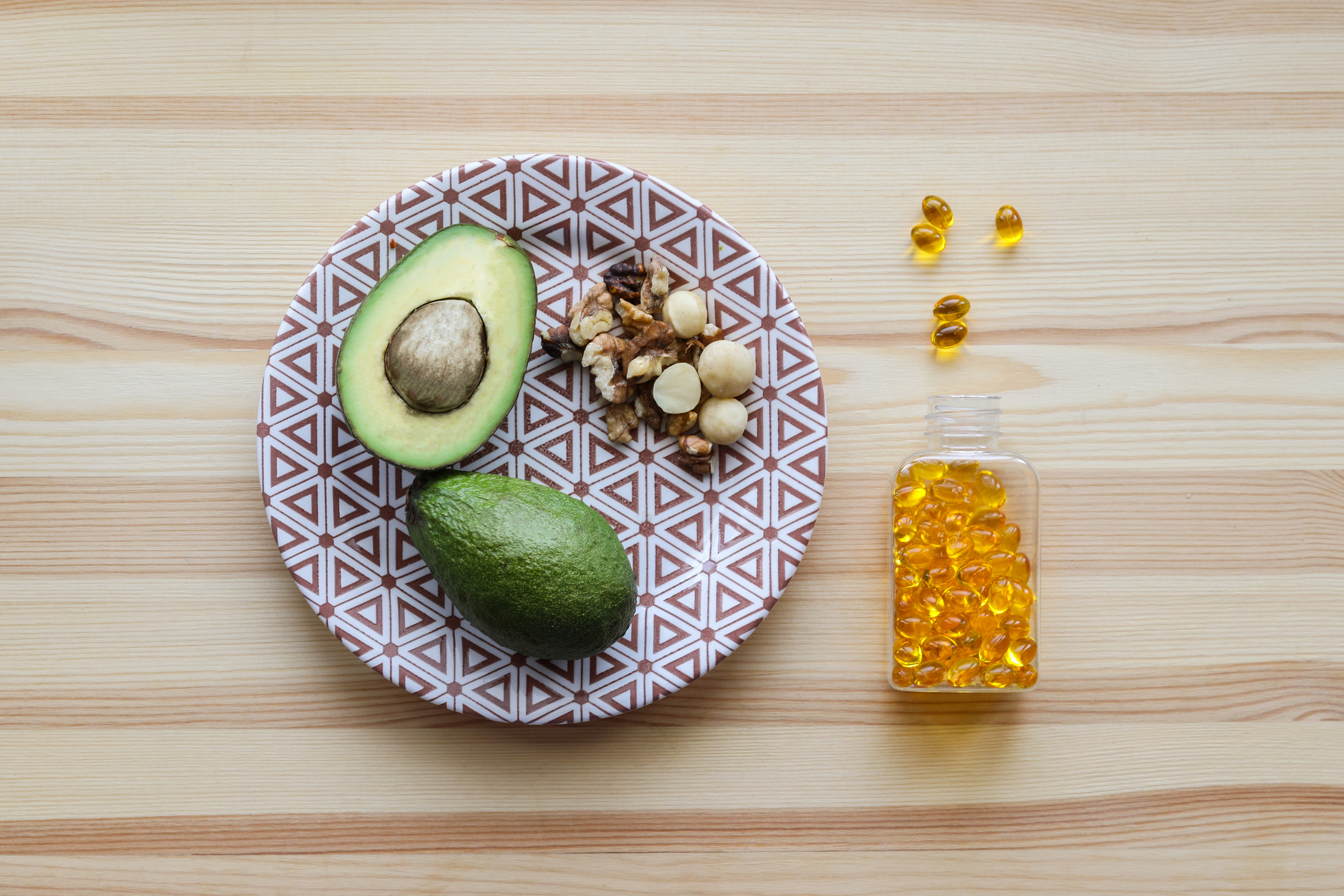 Plate with a halved avocado on it, nuts, and fish oil supplements to the side of plate.