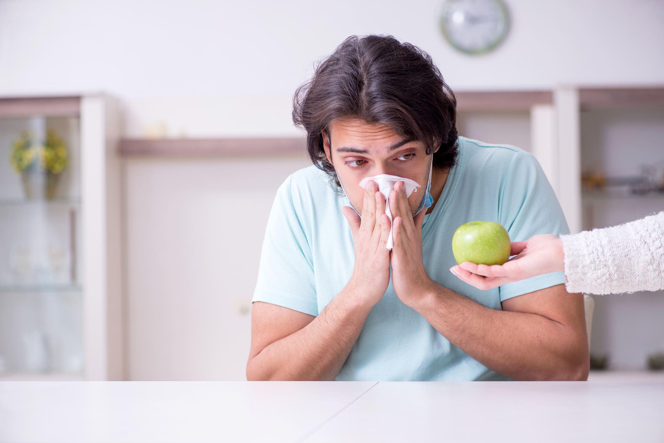 Young man looking at fruit and sneezing into a tissue.