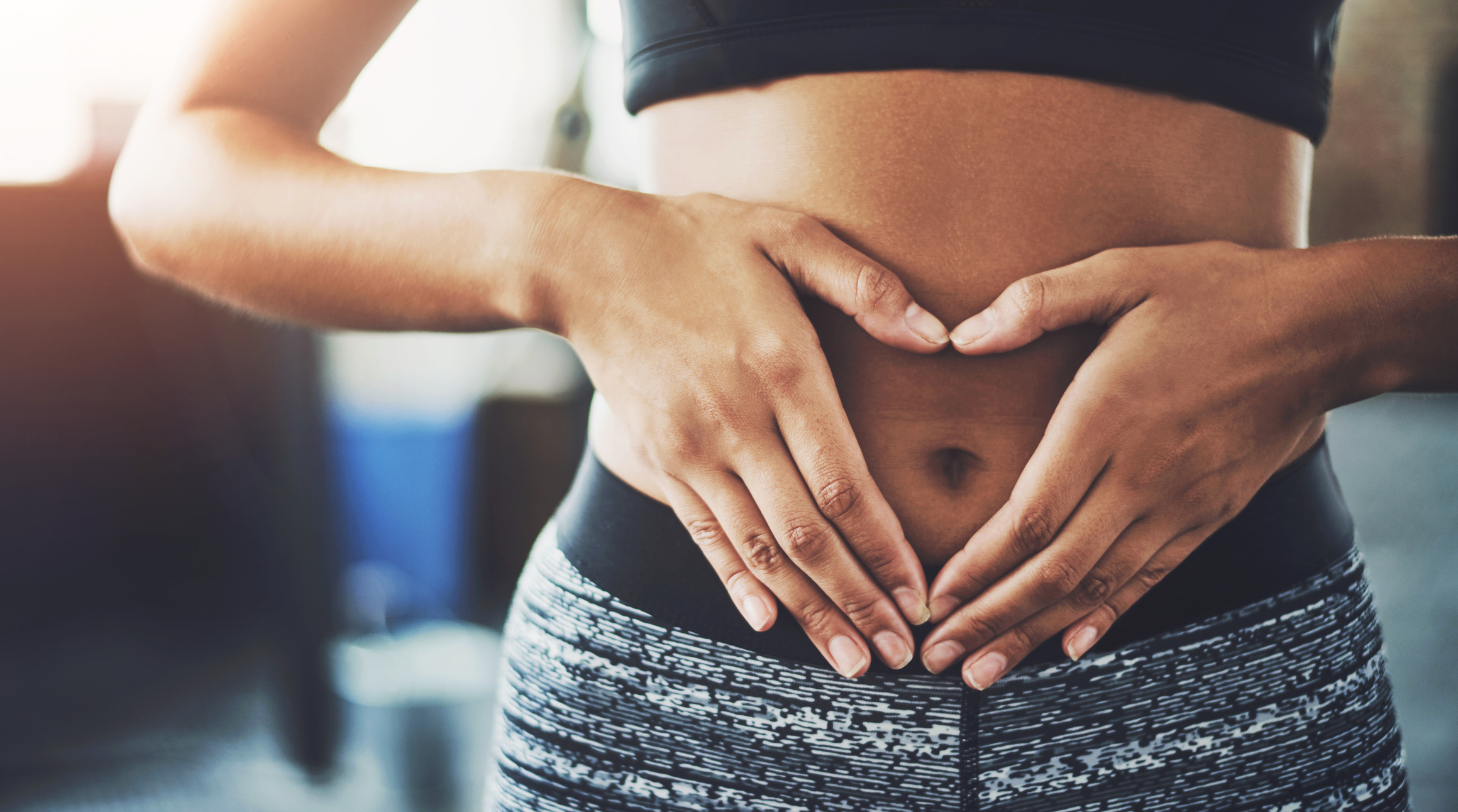 Woman with sports bra, using hands to create a heart over navel.