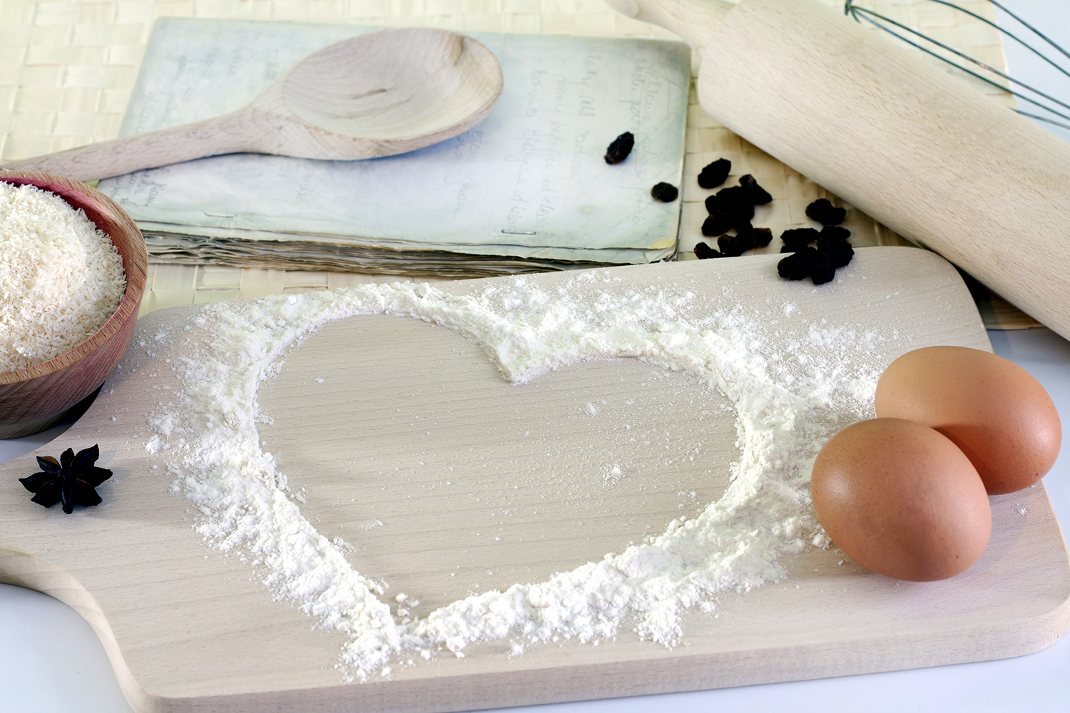cooking utensils, eggs, and flour on a cutting board in a heart design