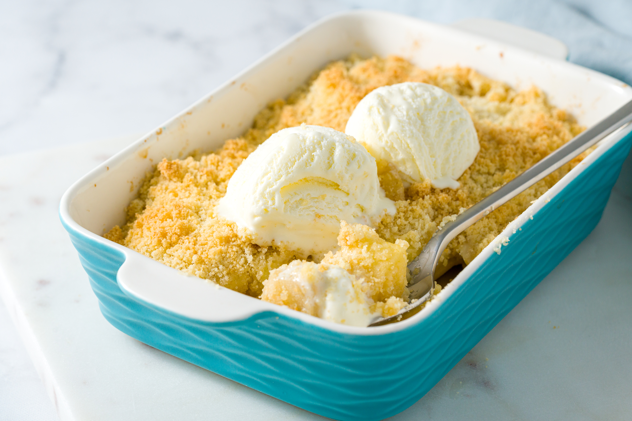 Aqua baking pan filled with fruit crumble with two small scoops of ice cream on top.