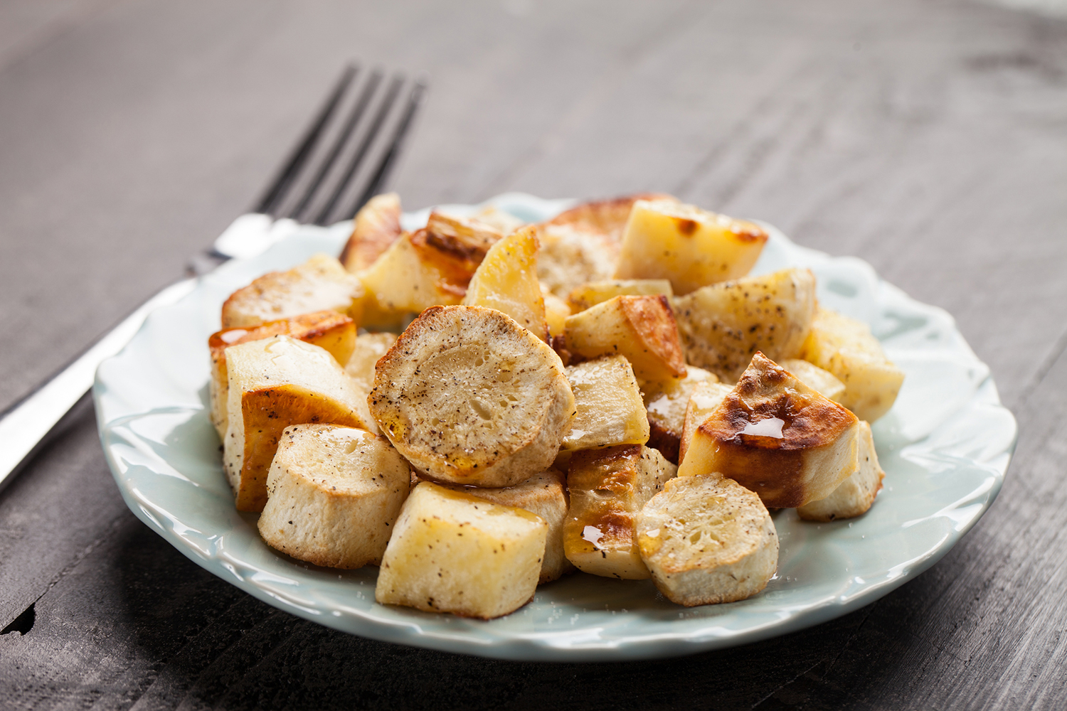 Roasted parsnips on a blue china plate on a dark wooden background.