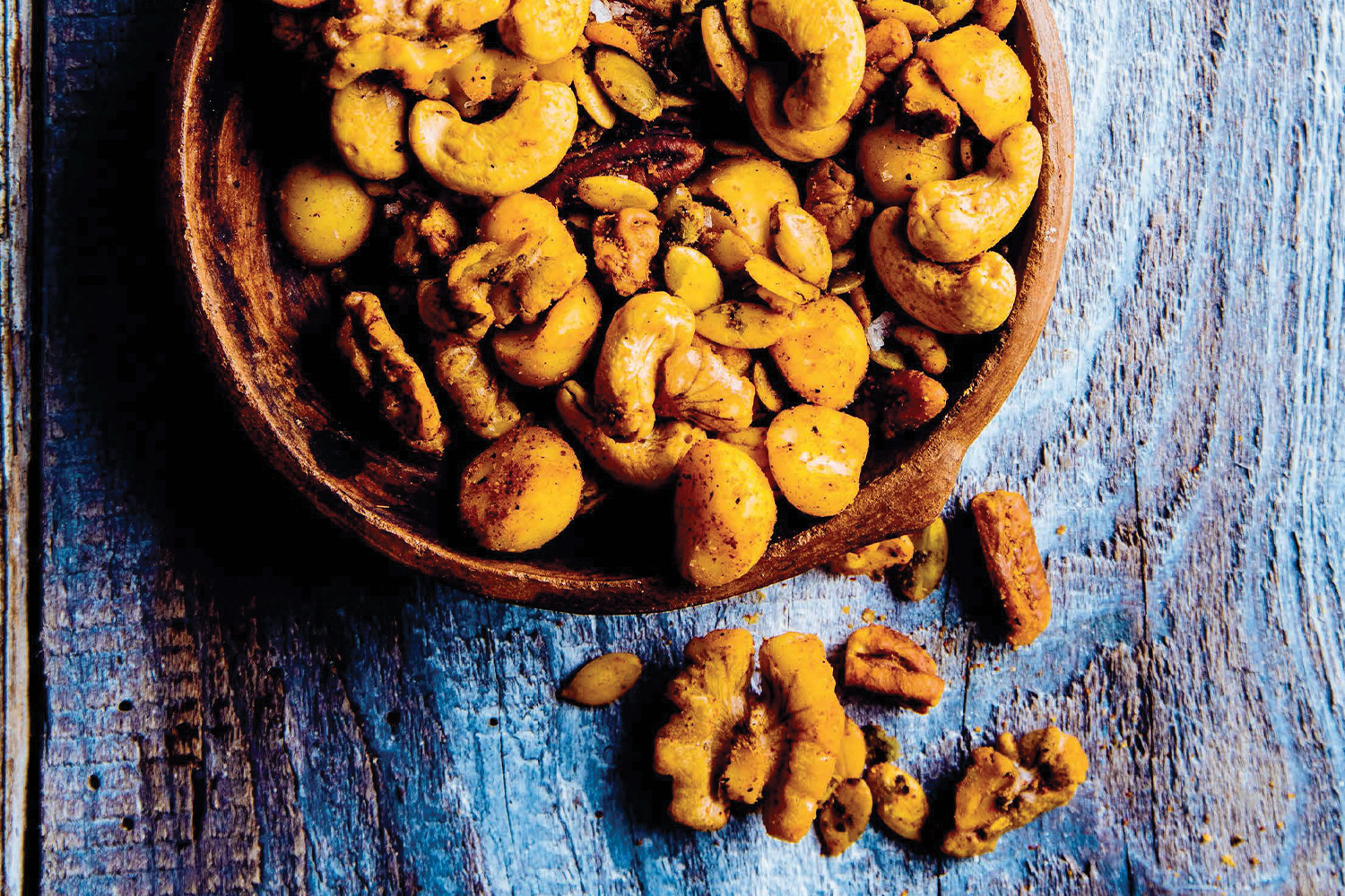 Taco-Spiced Mixed Nuts in a wooden bowl on a blue stained wooden table.