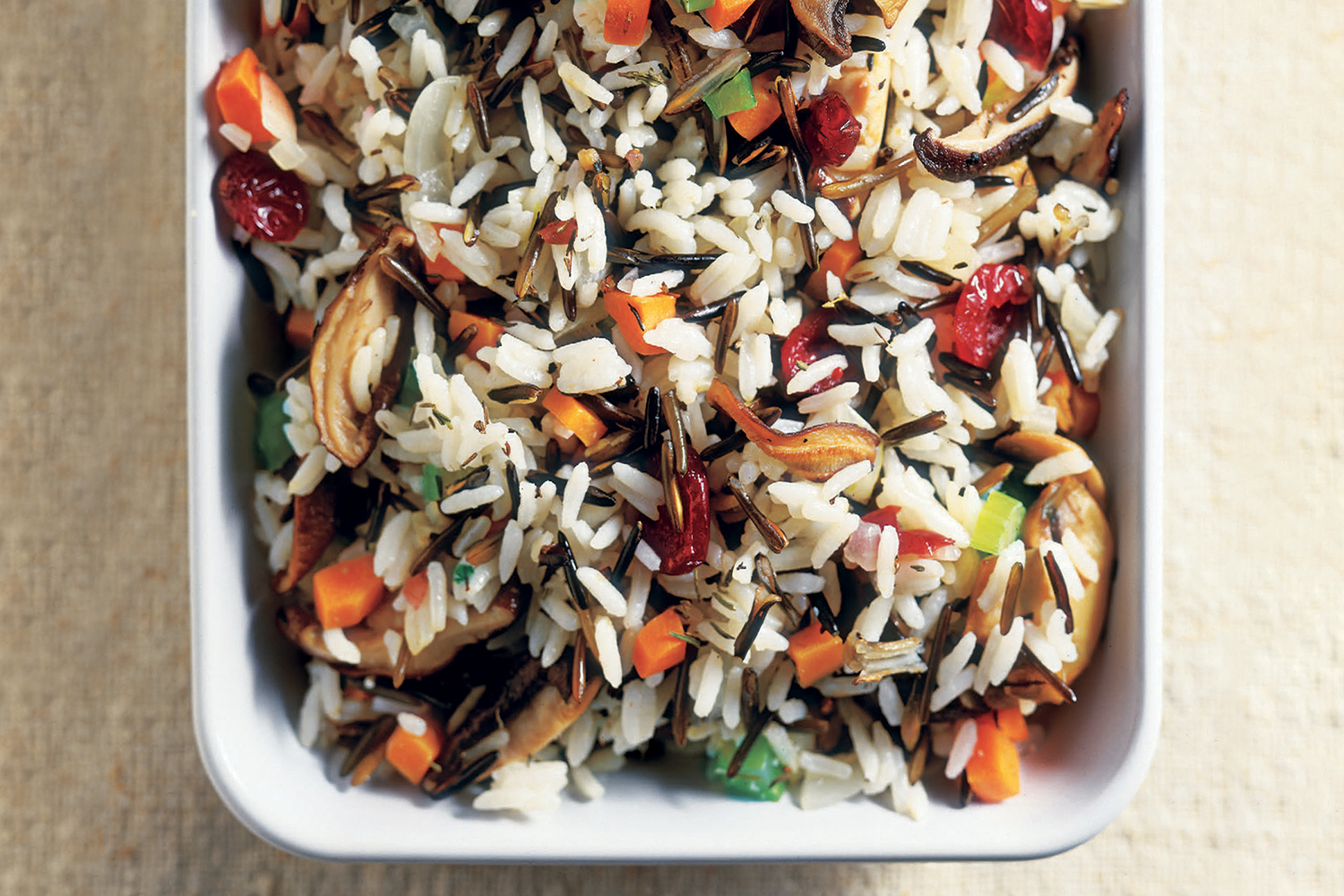 Wild Rice and Mushroom Stuffing in a white serving dish on a tan background.