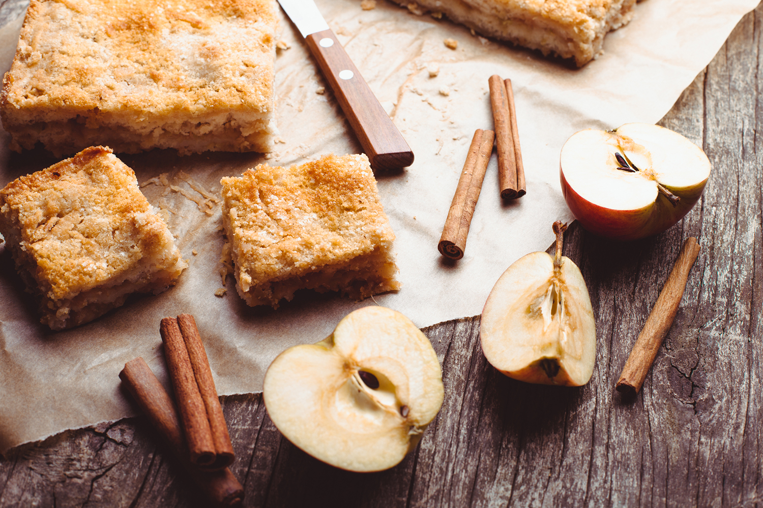 Apple cake with halved apples and cinnamon sticks on a rustic wooden table.