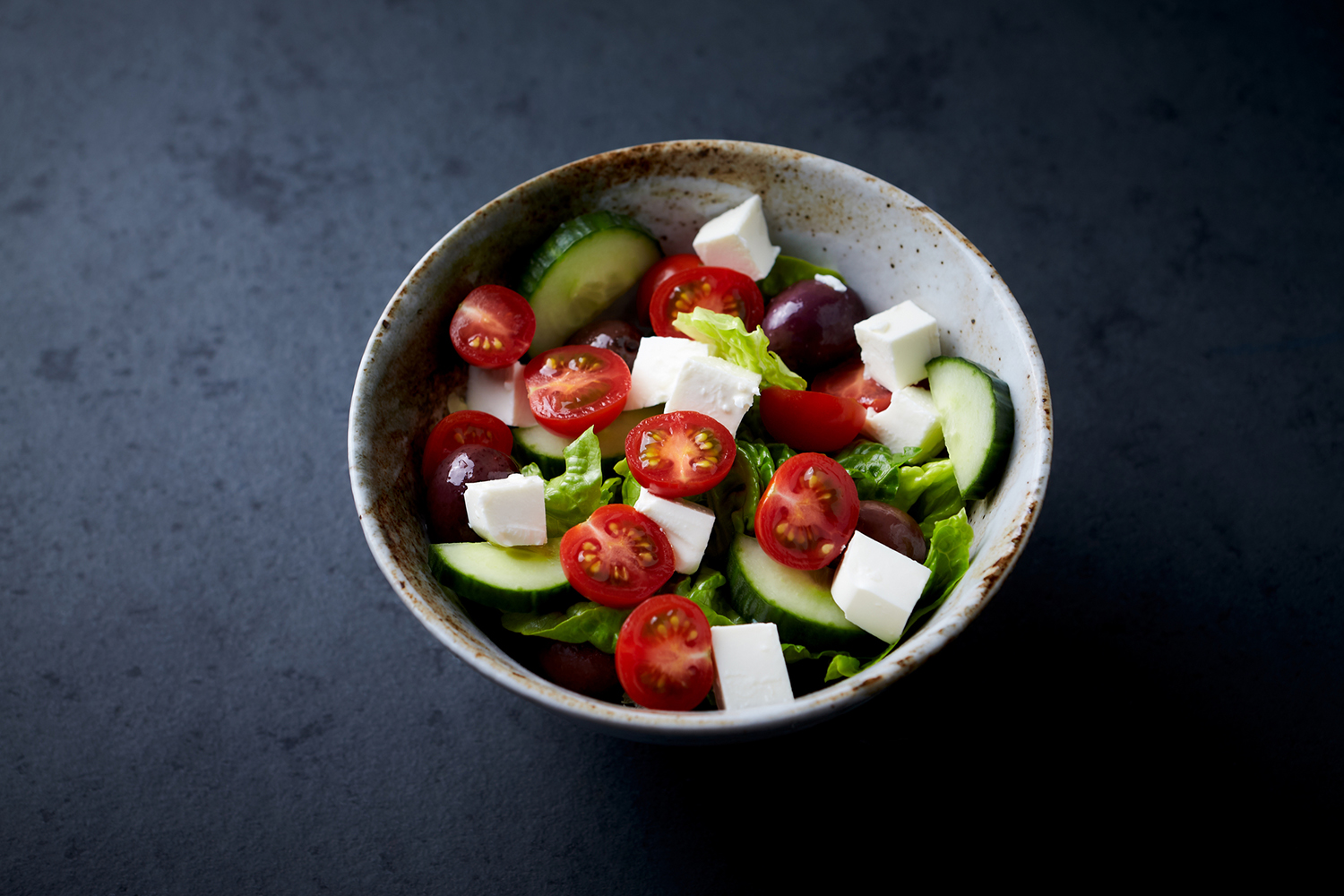 a bowl of greek salad with cucumbers, olives, and cherry tomatoes