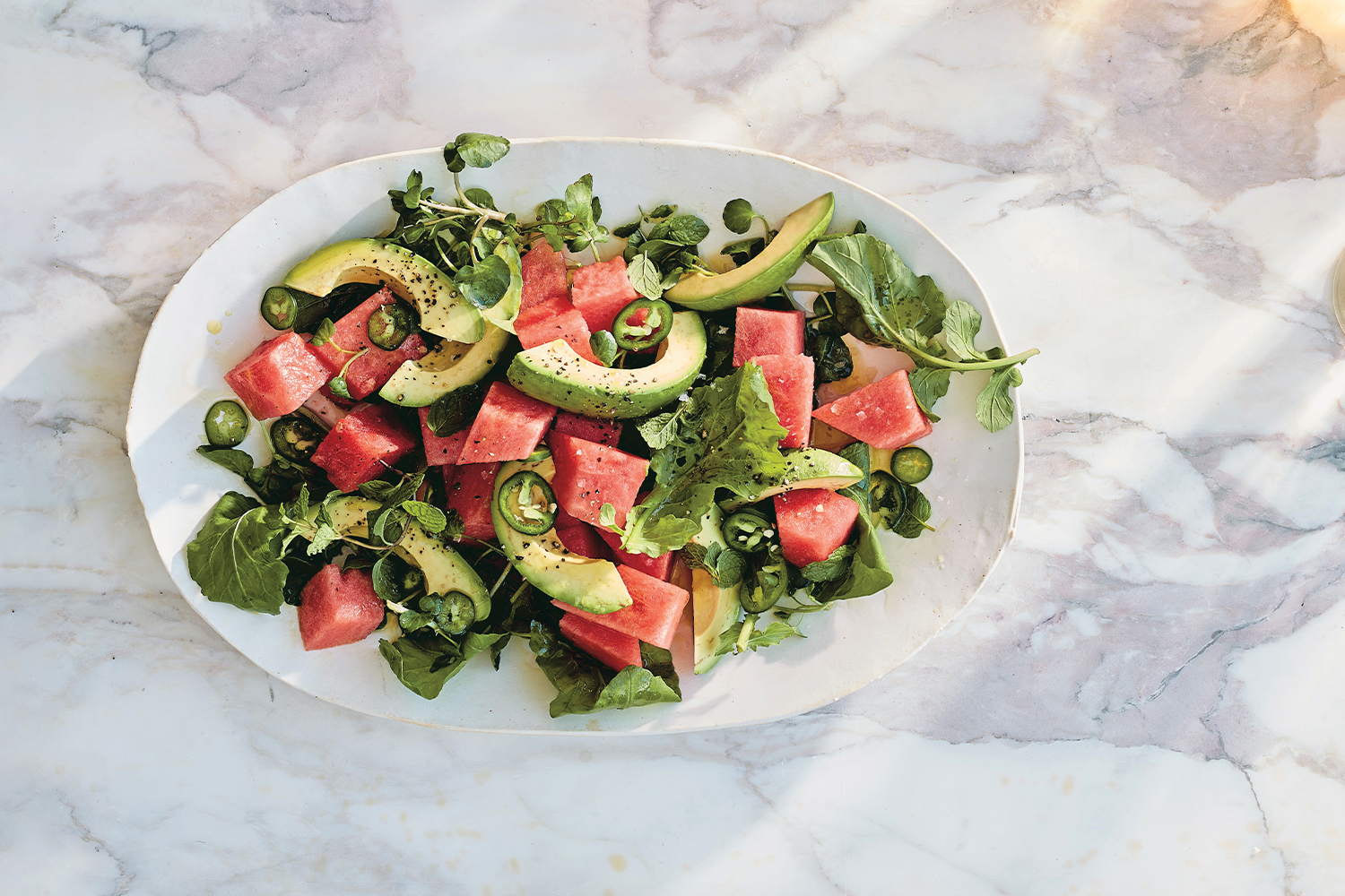 Top view of Spicy Watermelon Salad on a white platter on a white marble background.