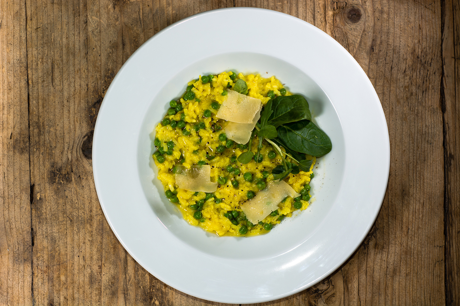 a bowl of risotto with leeks, peas, garnish, and cheese