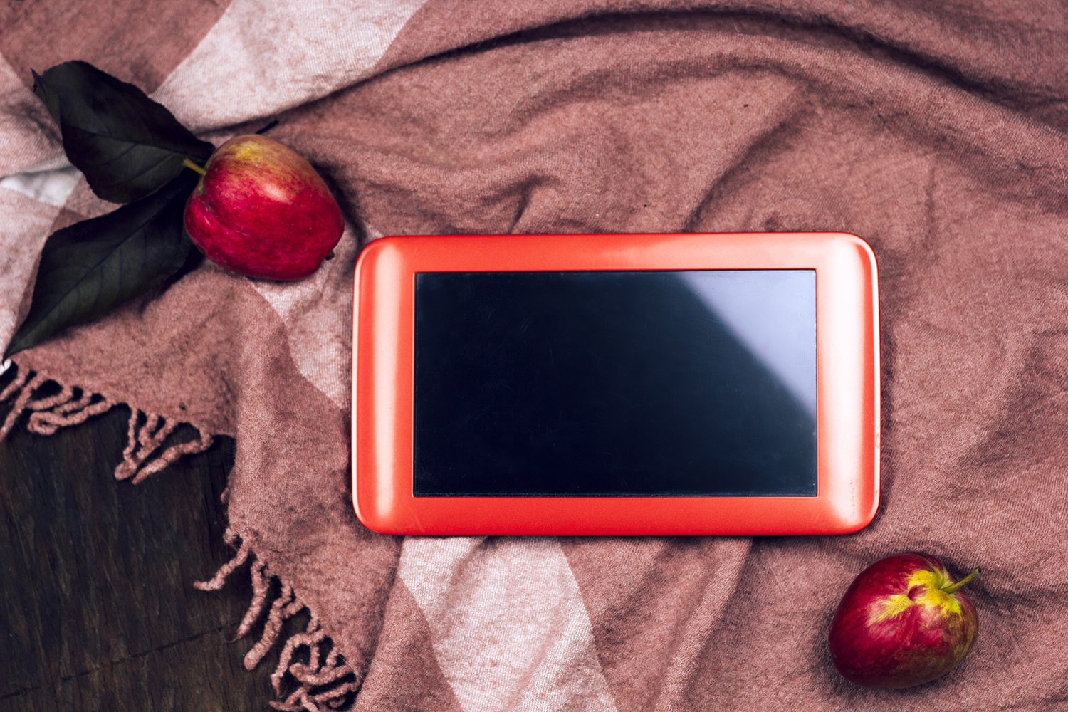 An IPad on a scarf with apples surrounding it.