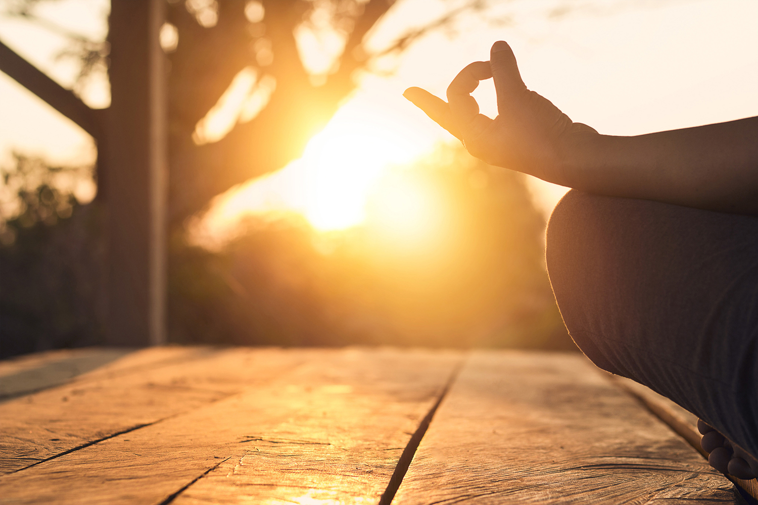 View of a woman's knee and hand in yoga pose, sunset in the background.