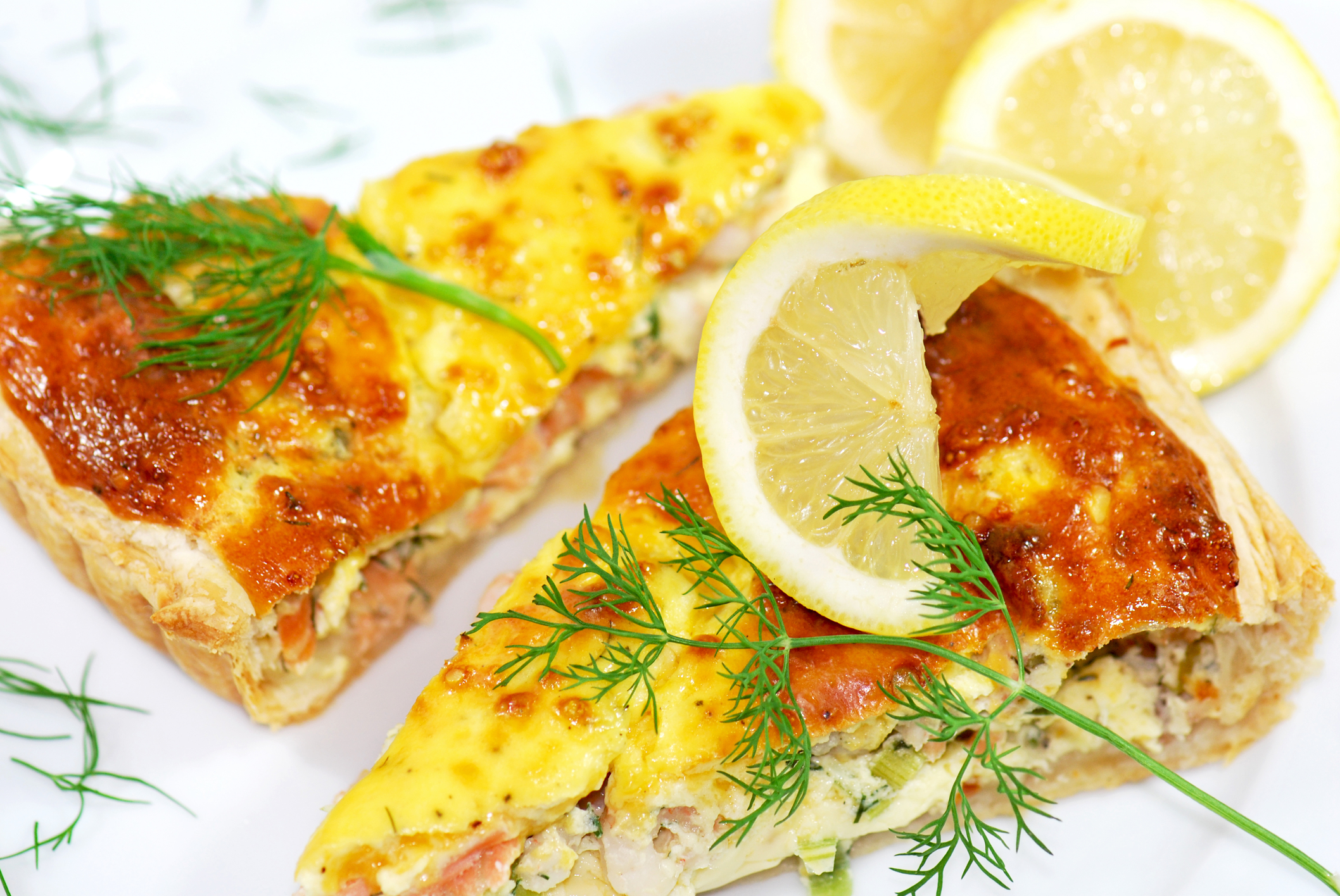 two slices of quiche, toped with sprigs of dill and a lemon wedge