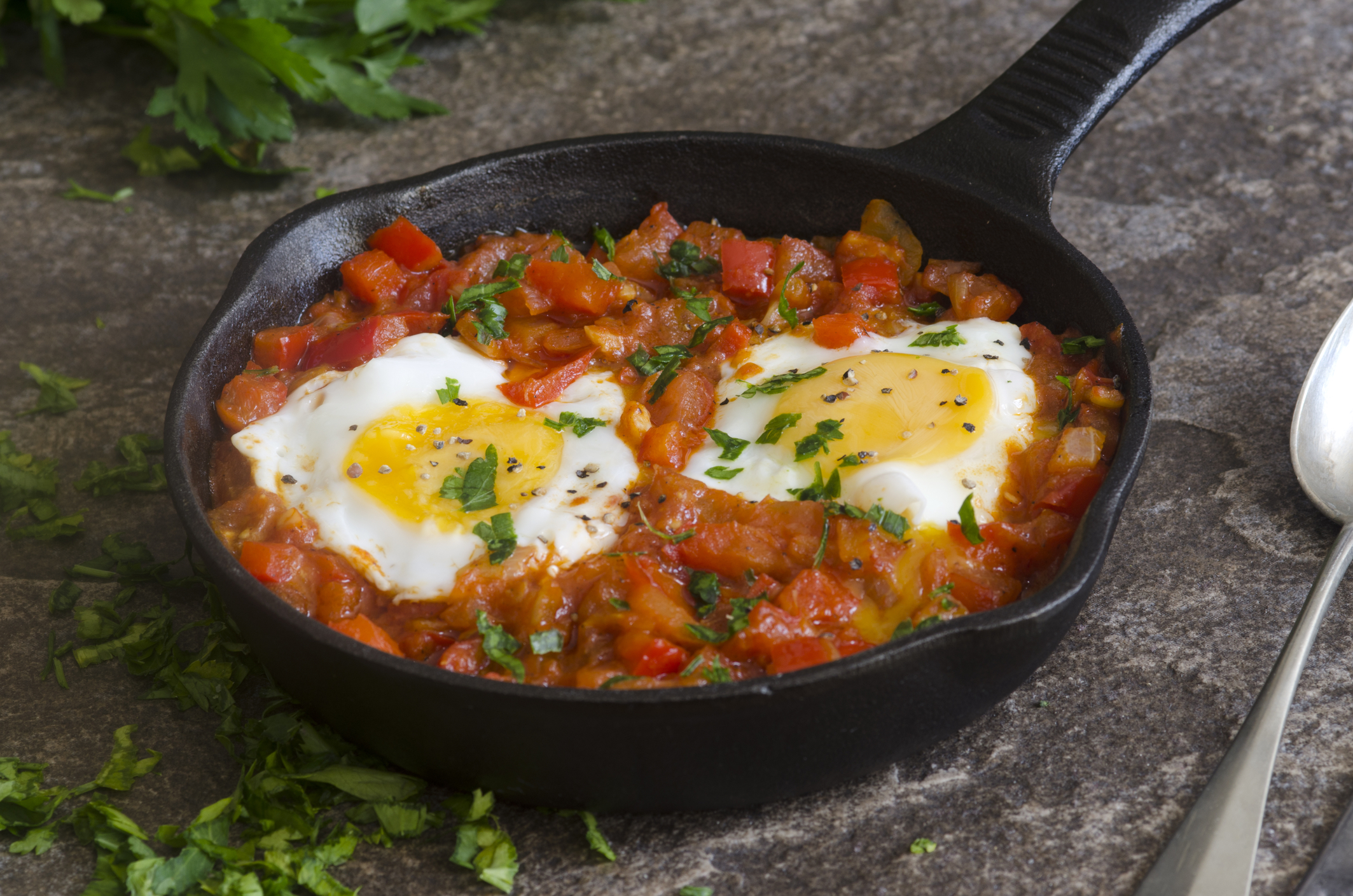 two eggs nestled in chopped tomatoes and red bell peppers in black skillet