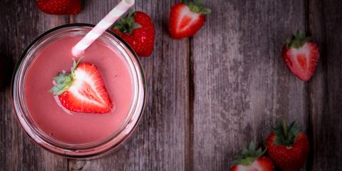 A glass of strawberry smoothie on weathered picnic table wood.
