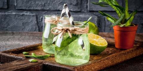 Aloe infused Lime water in drinking jars with black and white paper straws on a cutting board.