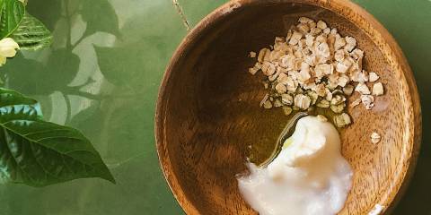 A top view of wooden bowl with oats, oil and yogurt on a green tile countertop.