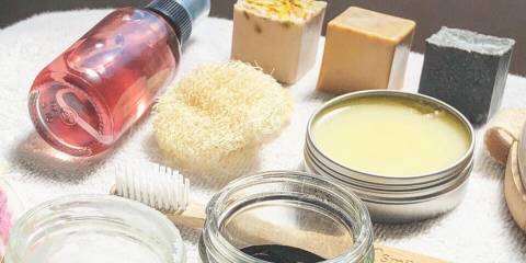 A variety of natural skin care products, soap bars, coconut oil, toner loofah, salves and more laid out on a whit towel.