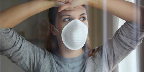 A woman in a face mask looking longingly out of a window.