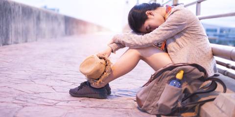 An exhausted asian woman sitting on a bridge with her head on her knees.