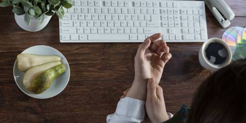 A woman massaging her inflamed wrist in front of a keyboard