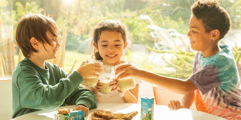 kids sitting around a plate of cookies, cheering with glasses of plant-based milk