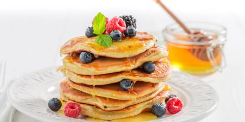 a stack of fluffy pancakes with berries and honey