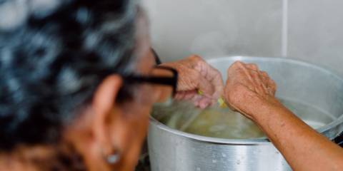 a grandmother putting cut-up vegetables into a boiling pot