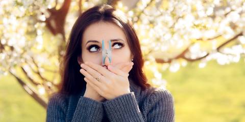 a woman outside sneezing with a clothespin on her nose