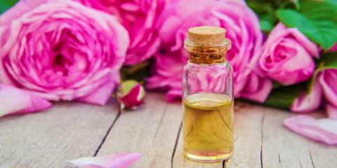Rose hip oil in a clear corked jar. Pink roses in the background.