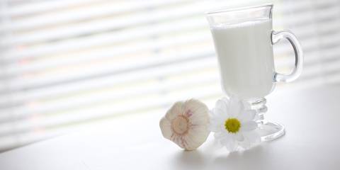 A glass of milk next to a clove of garlic and a fresh flower