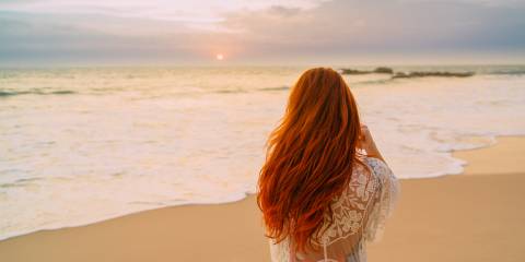 Red head woman on the beach looking at the sea.