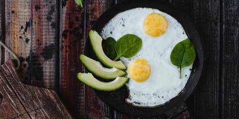 Fried eggs in a cast iron pan, with avocado slices garnished with spinach.