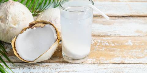 A glass with coconut water next to a coconut split in half. 