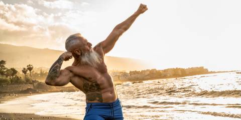 an old man flexing his impressive physique on the beach