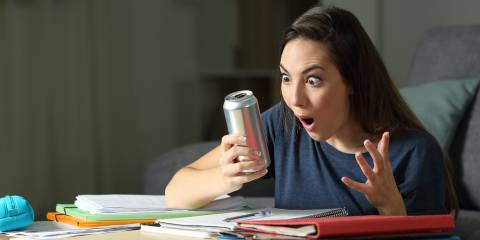 a young woman studying, looking at her energy drink can in surprise